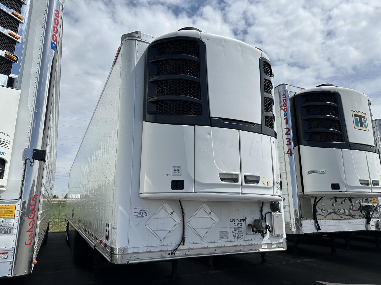 Vehicle trailer front view showing a white Great Dane air ride reefer with black cooling vents and rear doors, other trailers visible.