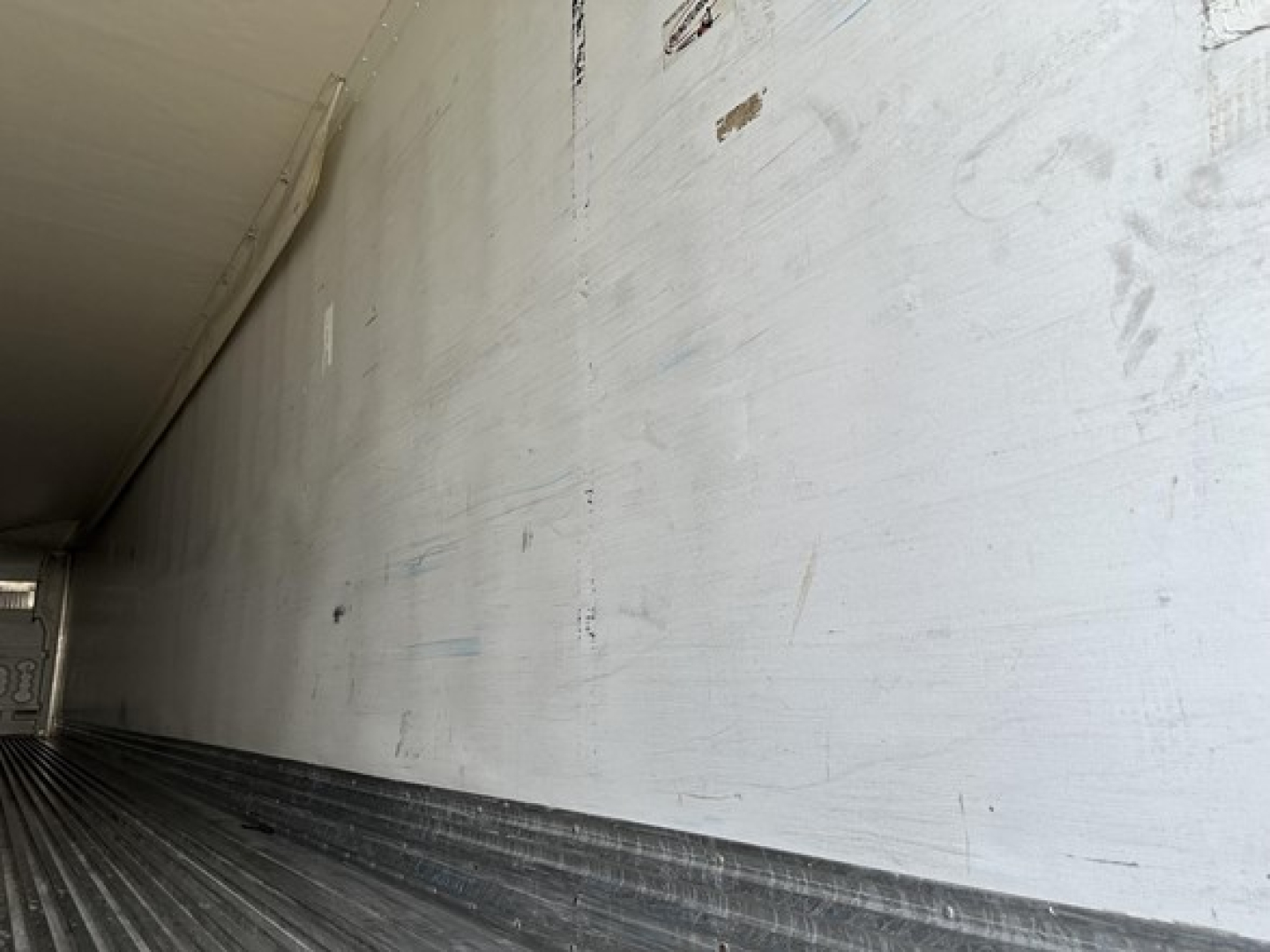 Trailer interior wall with faint markings and scratches, long white surface, dark ribbed floor visible at bottom.