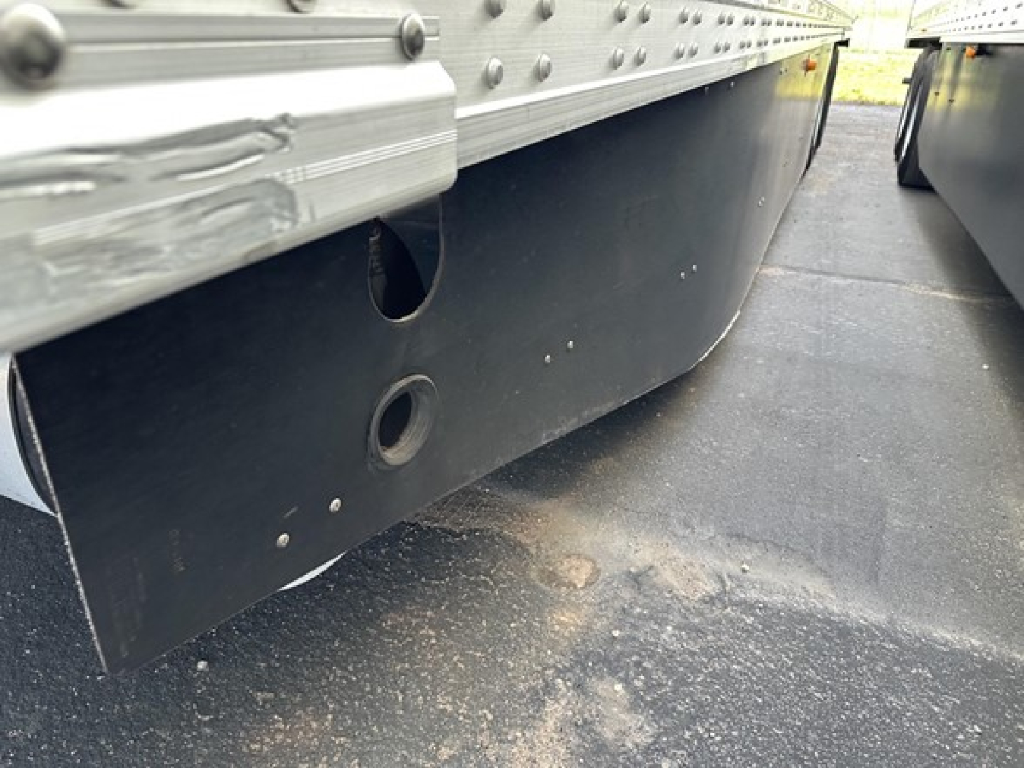 Trailer undercarriage showing lower side rail and mudguard with circular cutouts and riveted steel construction.