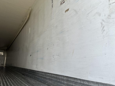 Trailer interior wall with faint markings and scratches, long white surface, dark ribbed floor visible at bottom.