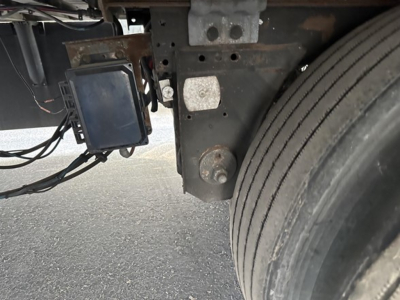 Trailer side showing a maintenance device mounted near the frame and a tire; electronics module with a display and wiring harness visible.