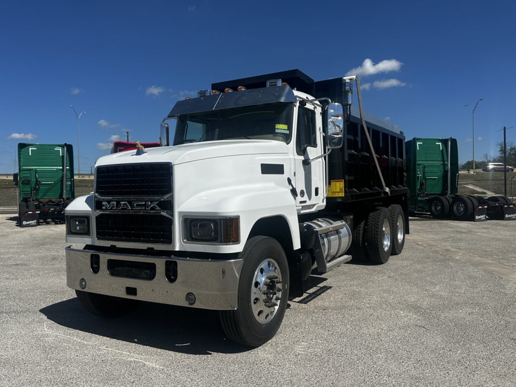 Dump truck front-left view showing white 2026 Mack PI64 with black grille, chrome bumper, dual rear wheels, and dump bed. VIN tag not legible.