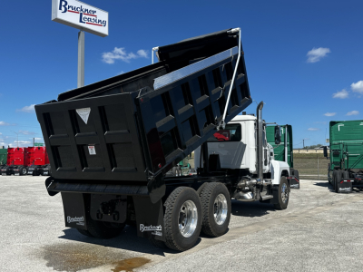 Dump truck bed raised showing cargo area and rear wheels of a Mack PI64 dump truck in a dealership lot.