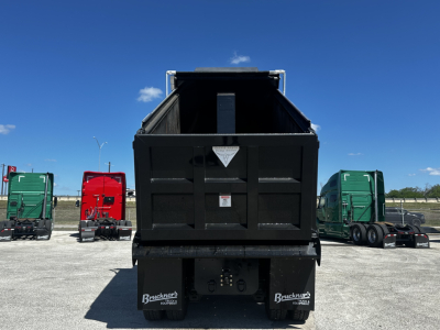 Dump truck bed of a 2026 Mack PI64 rear view showing cargo space, hydraulic lift, and rear bumper with mudflaps.