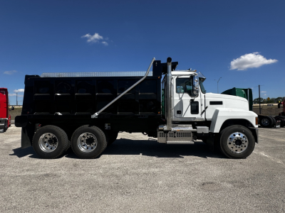 Dump truck side view showing Mack PI64 chassis with black dump bed and white cab, three rear axles, chrome steps, and hydraulic sides, no text visible on body.