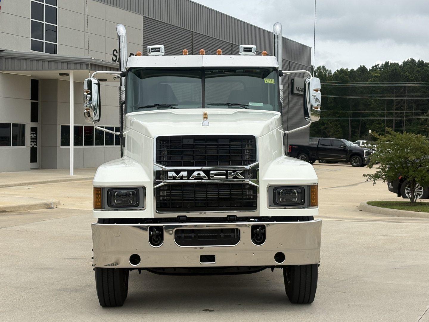 Front view of a white 2027 Mack PI64T truck with large grille, bumper, and side mirrors. Emblems visible: MACK on grille.