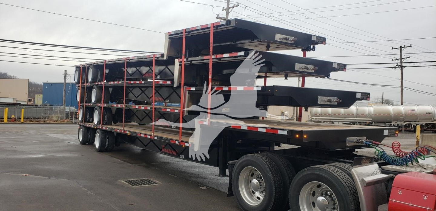 Transcraft Dtl-2100 drop deck trailer with stacked decks and red straps, dual rear axles visible.