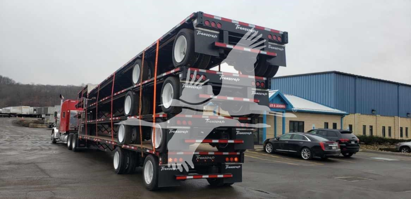 Trailer deck stacked with multiple wheels on a Transcraft DTL-2100 lowboy trailer showing rear ramps and tandem axles.
