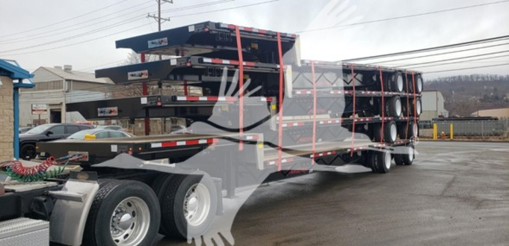 15000 lb dual-axle drop deck trailer with multiple steel flat racks and spare tires stacked on the trailer; visible text on side not legible
