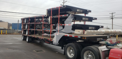 Transcraft Dtl-2100 drop deck trailer with stacked decks and red straps, dual rear axles visible.