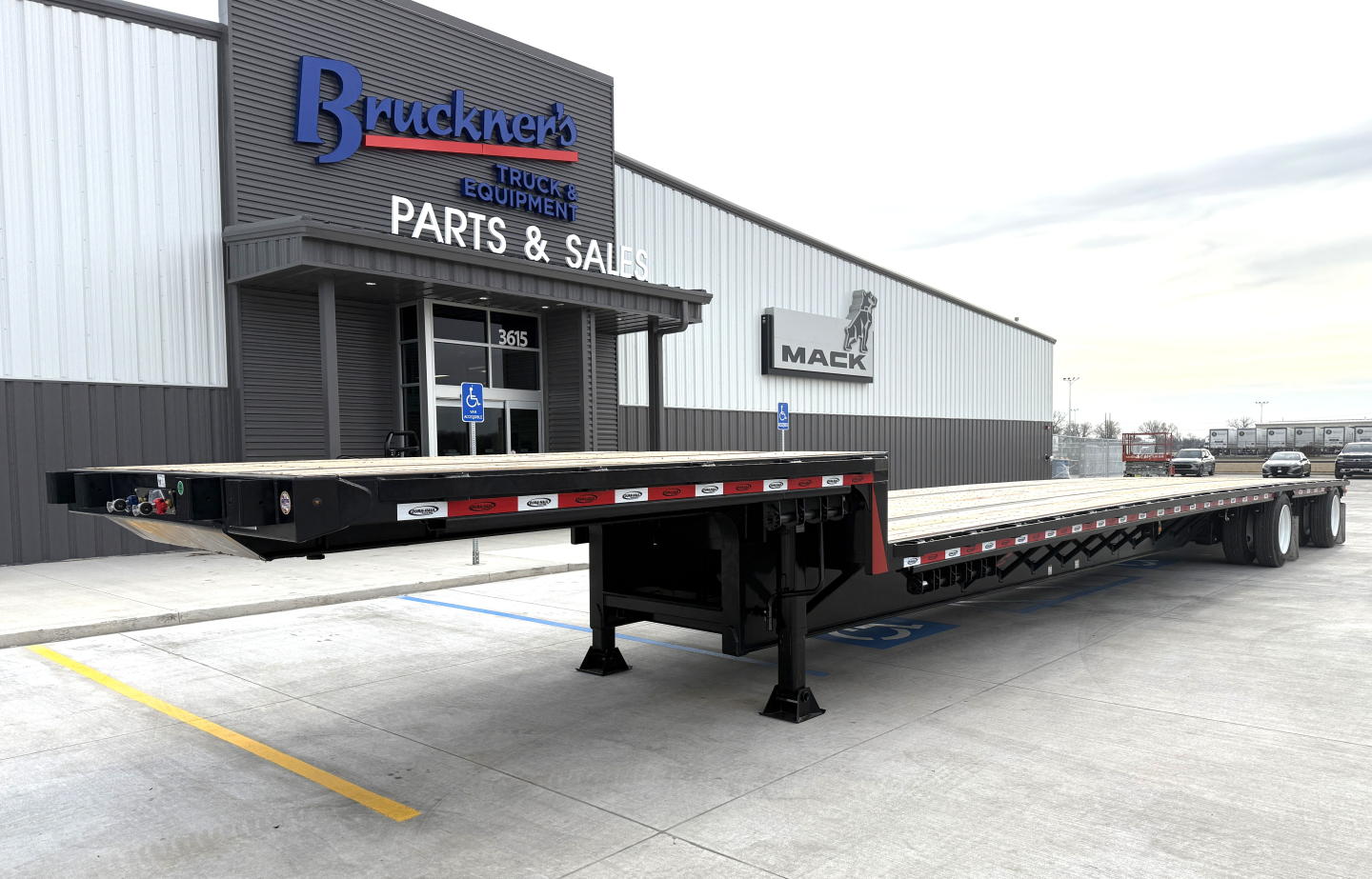 Flatbed trailer showing a 48-foot drop deck spread configuration with black frame and red-white reflective safety decals, parking at a parts and sales facility.
