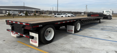 Flatbed trailer showing 48-ft Dura Haul drop deck with black frame and white wheels, new condition, long chassis with front cab and rear tail, stock number decals visible.