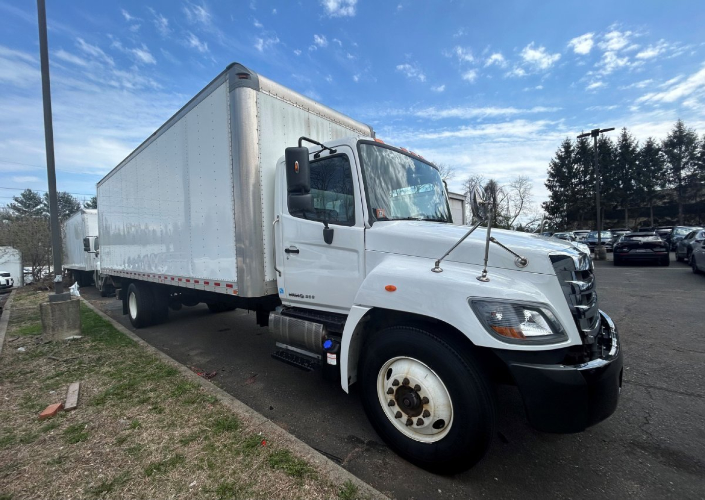 Box van truck with white cab and long white box, front passenger-side view, chrome grille, dual mirrors, on a parking lot.