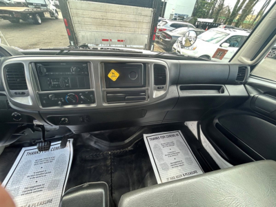 Cab interior of 2020 Hino 338 cargo box van showing dashboard with HVAC controls, radio, and center stack; front windshield and parking lot visible through windshield.
