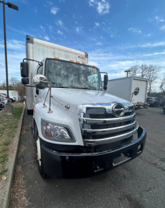 Front view of a white 2020 Hino 338 box truck showing chrome grille, Hino emblem, large side mirrors, and cargo box in background.