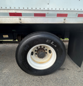 Hino 338 truck wheel and underside showing M+S 225/75R16E tire, white steel wheel, undercarriage and side panel of box truck.