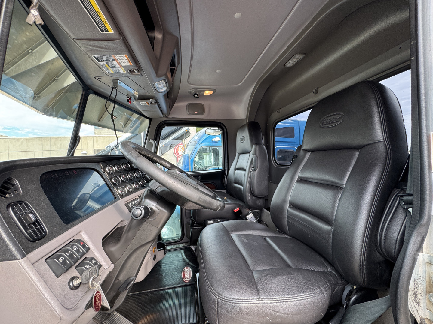Peterbilt 389 truck cabin interior showing driver seat and dashboard with steering wheel, instrument cluster, and overhead controls.