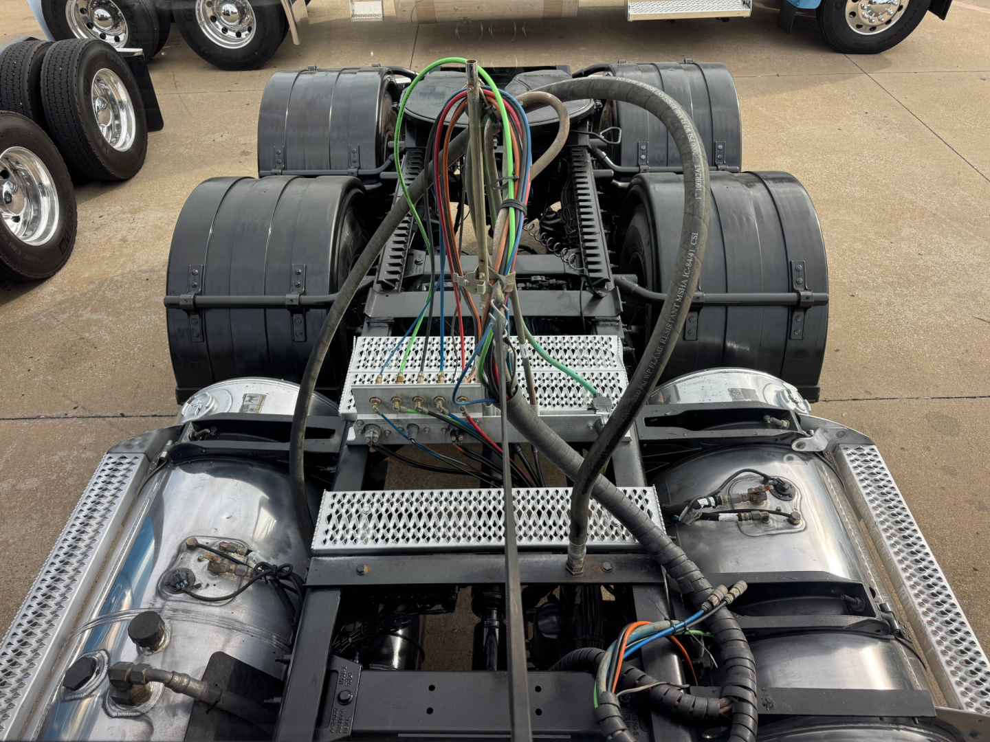 Peterbilt 389 chassis with exposed wiring harnesses and dual fuel tanks; view from rear showing fifth wheel area, steps, and air lines; no cab image text visible.
