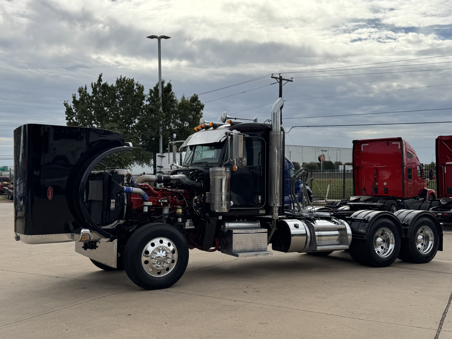 Peterbilt 389 conventional daycab tractor with hood open, showing engine bay and chrome fuel tanks.