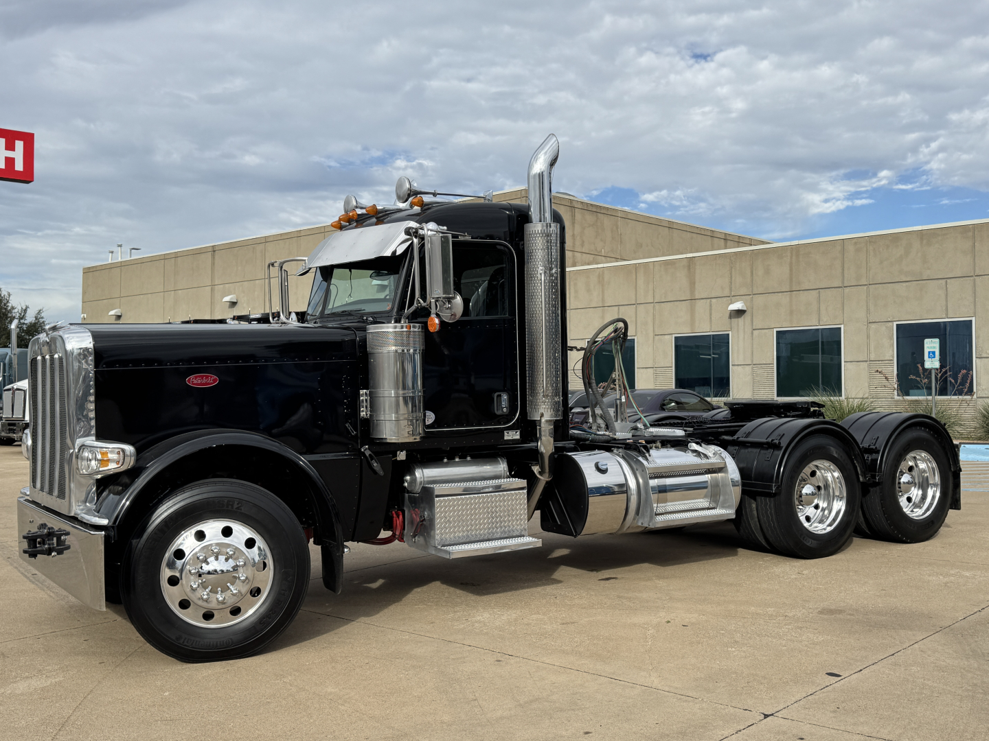 Peterbilt 389 conventional daycab truck in black with chrome exhaust stacks and dual rear axles, side view.