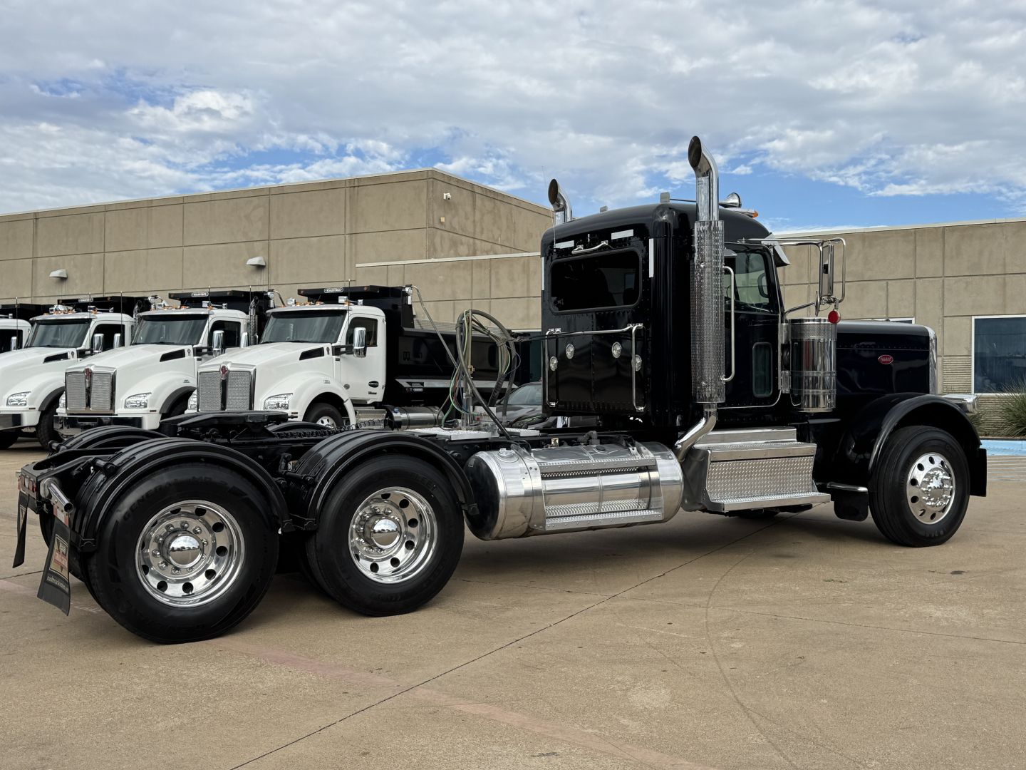 Peterbilt 389 conventional daycab tractor in a used condition, side view showing dual rear axles, chrome fuel tanks, exhaust stacks, and black cab with silver steps.