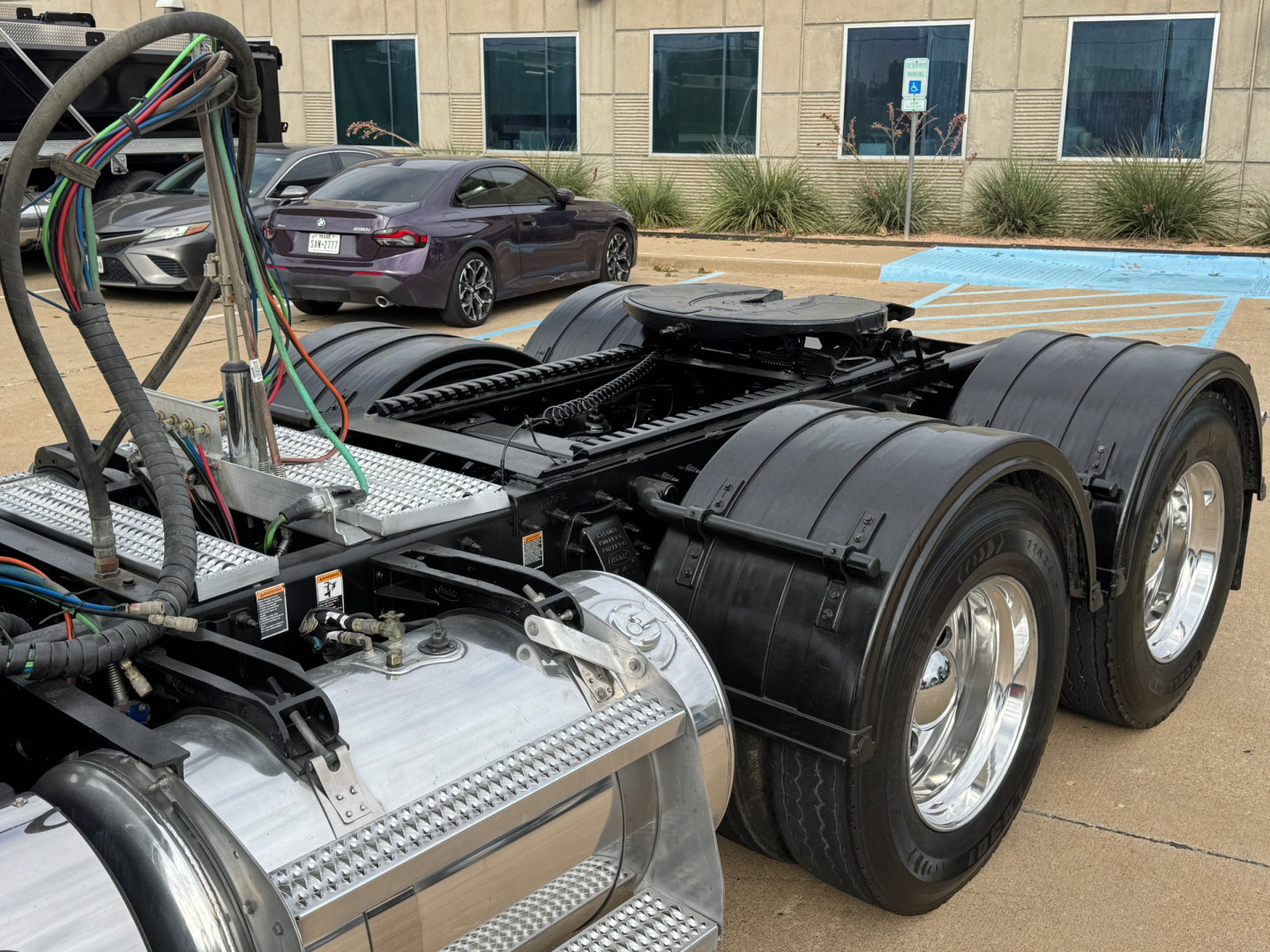 Peterbilt 389 tractor chassis showing rear dual drive axles and aluminum fuel tanks with wiring harnesses in foreground