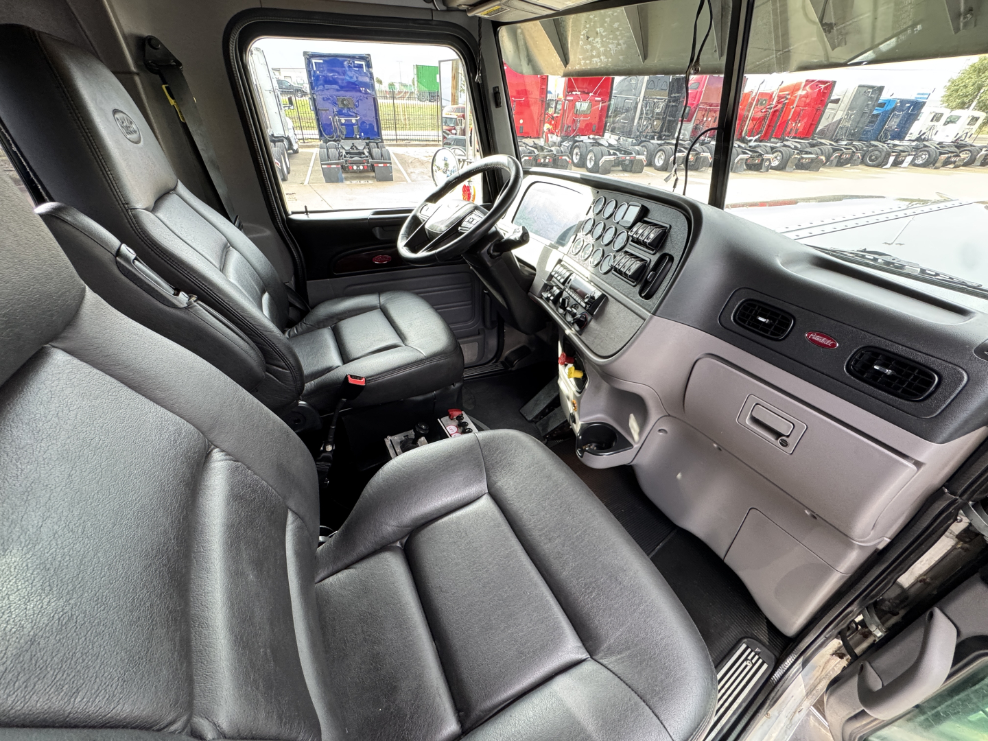 Truck cab interior with driver and passenger seats, steering wheel, dashboard, and center console visible.