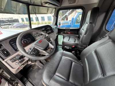 Peterbilt 389 cab interior showing steering wheel gauges and driver's seat with control panel and view through side window.