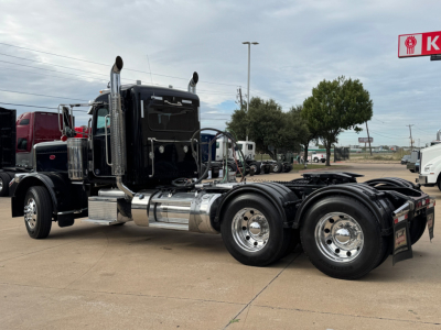 Peterbilt 389 conventional daycab tractor in a used truck lot, low-angle side view showing dual rear axles and chrome exhaust stacks.