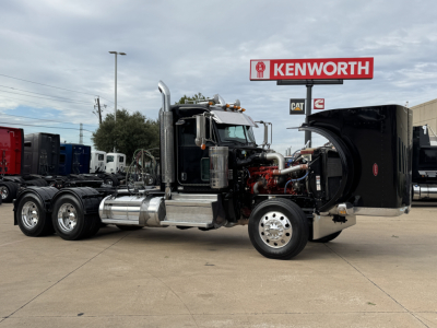 Peterbilt 389 conventional daycab truck in a dealership lot with hood open showing engine exposure and chrome exhaust stacks.