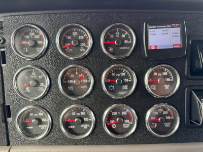 Peterbilt 389 truck dashboard cluster with multiple gauges and a small digital display showing weight summary, in-service status visible.