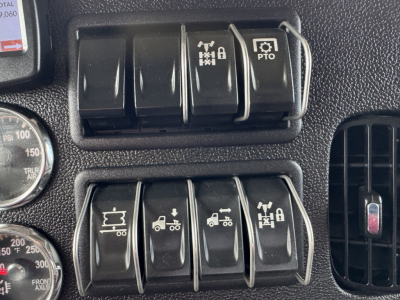 Dashboard switches and gauges in Peterbilt 389 cab showing multiple control levers and icons for PTO and other functions.