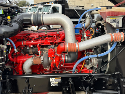 Peterbilt 389 engine bay showing red diesel engine with large aluminum intake pipe and blue hoses.