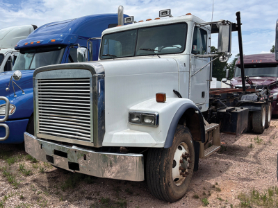 White Freightliner FLD120SD single-axle semi-truck cab shown in a used truck lot, front grille, large bumper, side mirrors, and a chassis behind the cab.