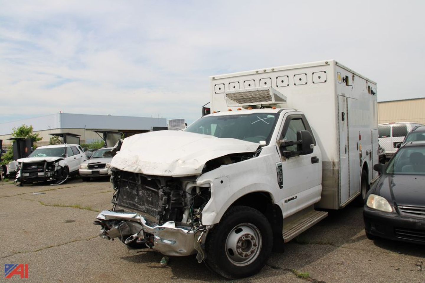 Front view of a damaged 2017 Ford F-350 Super Duty ambulance with heavy front-end impact, large chrome bumper and ambulance box behind cab, in a lot with other vehicles.