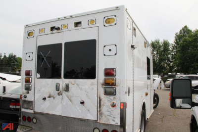 Ambulance rear view showing double doors, emergency lighting, and reflective panels with some dirt on white body.