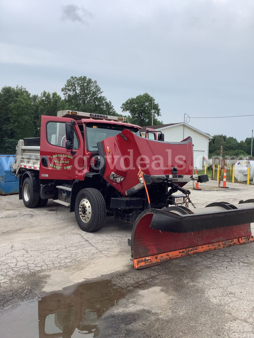 Freightliner 108SD dump truck in service showing front plow blade and dump bed, red cab with yellow lettering, stock photo of used vehicle.