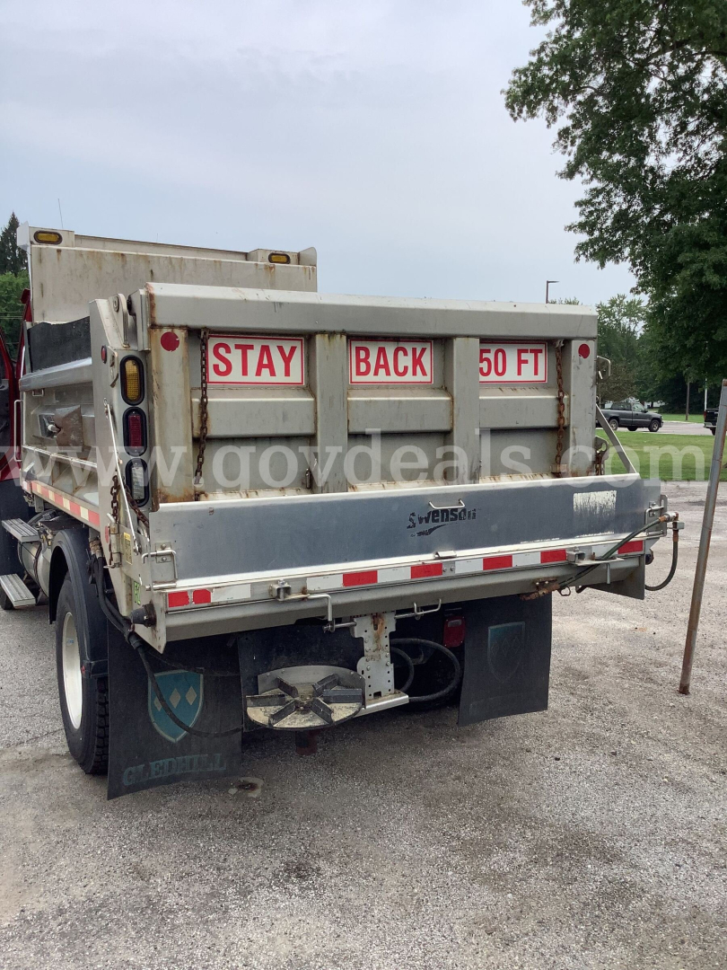 Rear view of a used 2013 Freightliner 108SD dump truck showing the dump bed with taillights, rear bumper, and warning sign 'STAY BACK 50 FT' on the tailgate.