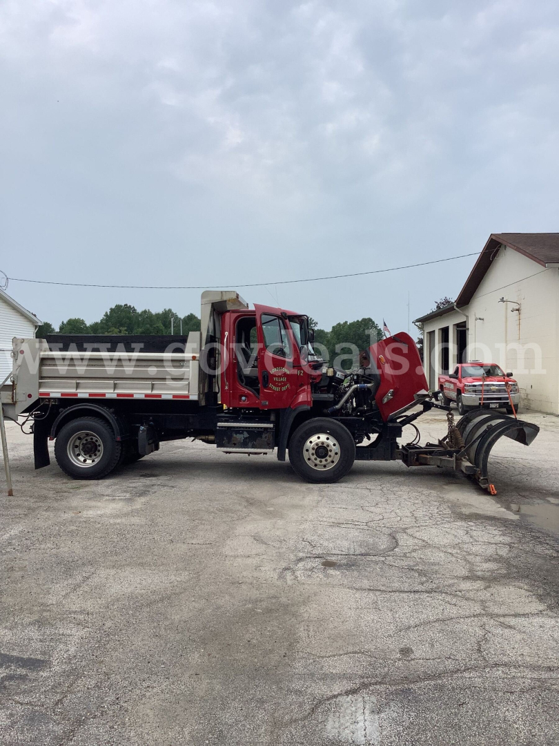 Freightliner 108SD dump truck side view showing front cab and dump bed with plow apparatus attached.