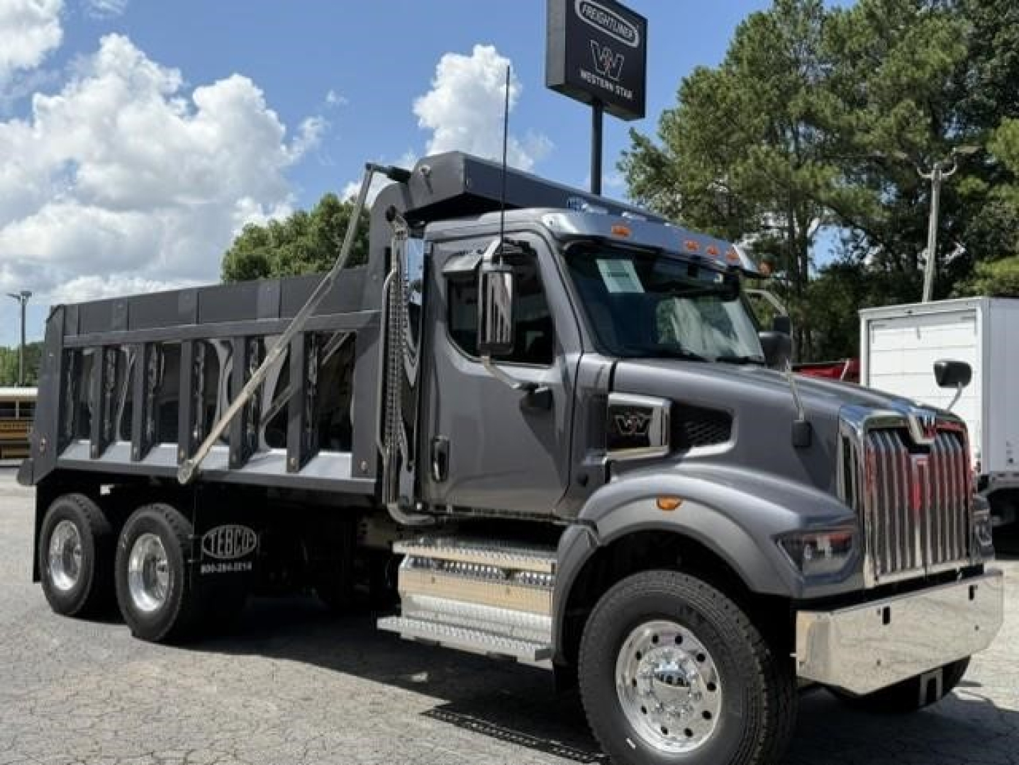 New Western Star 47X dump truck in profile view showing gray cab, dump bed, chrome grille, dual rear axles and Silverado-like emissions. Stock and VIN not visible.
