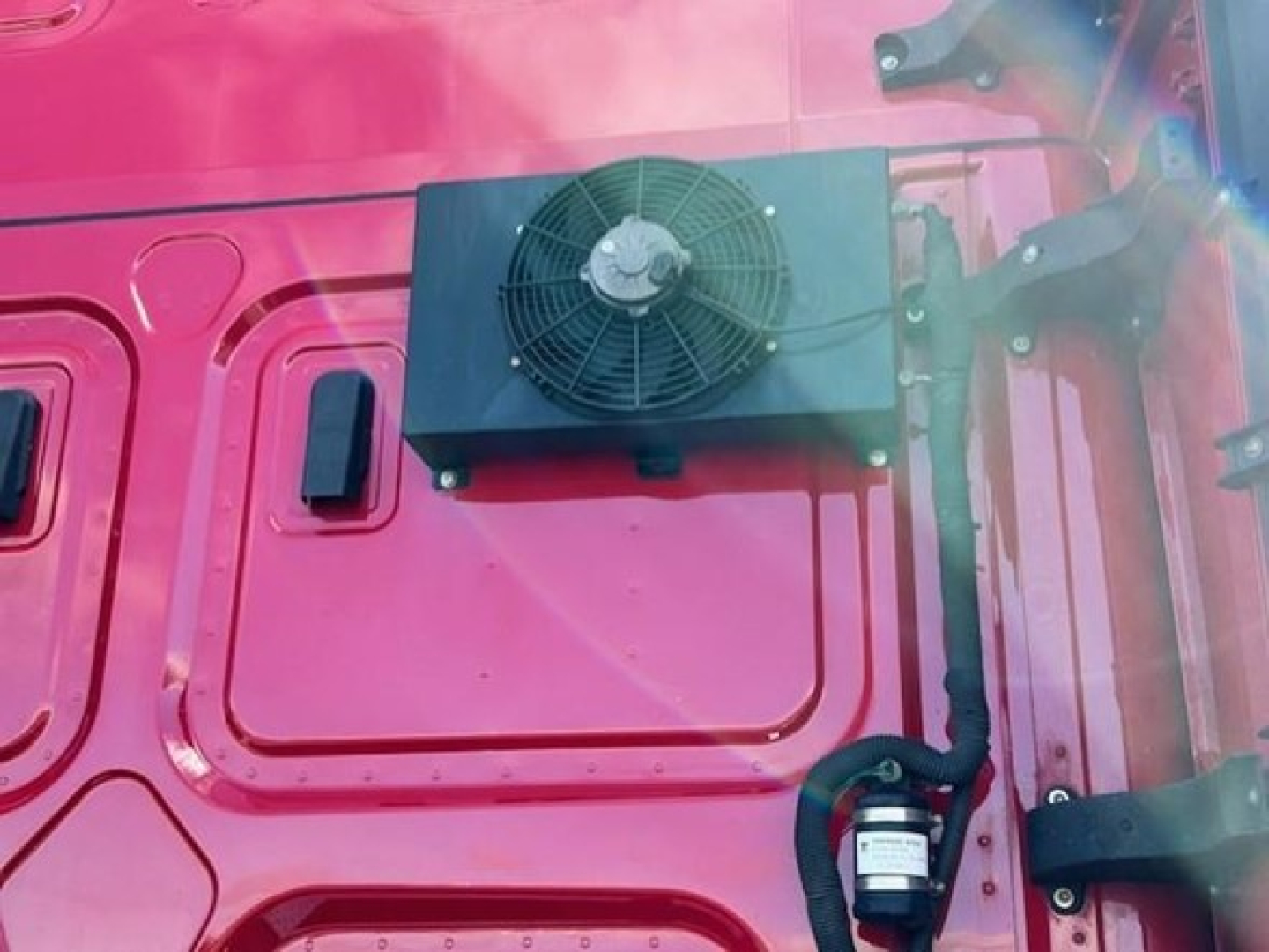 Truck engine bay or exterior cab area showing a mounted radiator cooling fan assembly on a pink Freightliner Cascadia 126 cab.