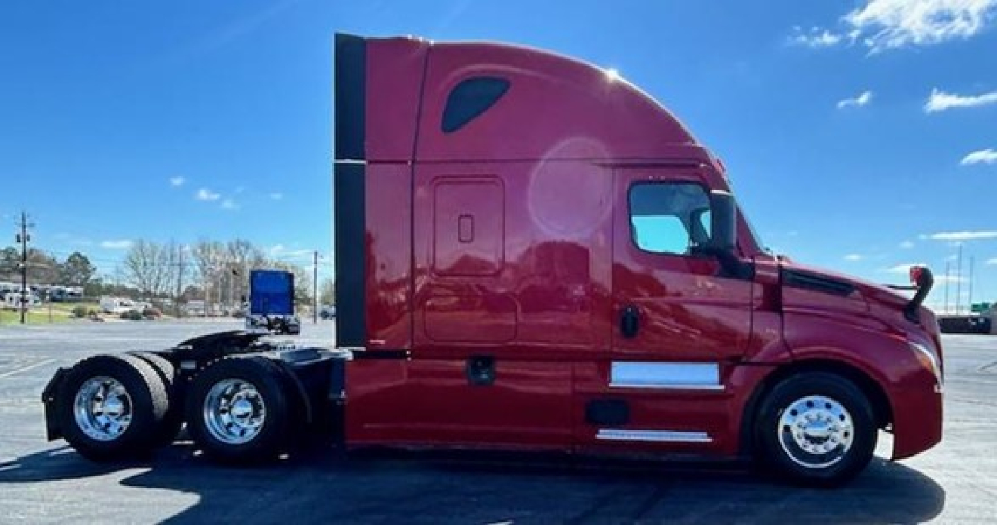 Truck side view of a red 2023 Freightliner Cascadia 126 sleeper cab showing chrome wheels and dual rear axles.