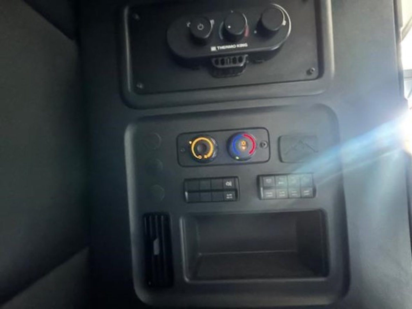 Truck cabin control panel with knobs and vents in a Freightliner Cascadia sleeper cab interior showing climate controls and storage compartment.