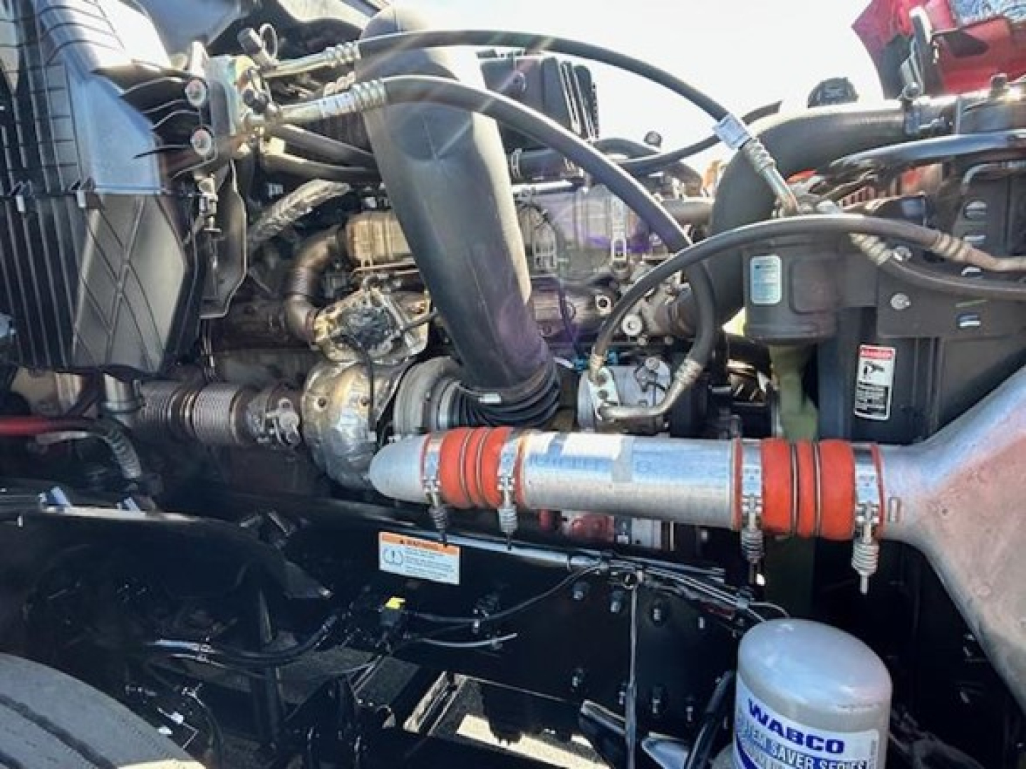Engine bay of a Freightliner Cascadia showing intake, hoses, and turbo components with orange coolant/heater hose clamps.