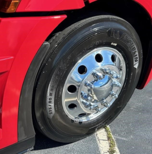 Truck wheel and front fender of a red Freightliner Cascadia 126 showing polished chrome hub with lug nuts and tire.