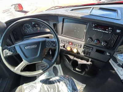 Interior view of a Freightliner Cascadia 126 dashboard with steering wheel, analog gauges, central touchscreen, and control panel.