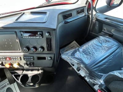 Freightliner Cascadia 126 interior dashboard and front passenger seat with plastic-wrapped seat and center console, gauges, vents, and cup holders.