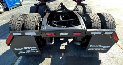 Rear view of a Freightliner Cascadia truck chassis showing dual rear axles and landing gear, with mud flaps labeled SelectTrucks and contact number.