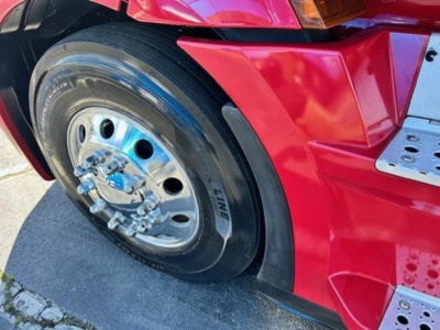 Truck wheel and front fender of a red 2023 Freightliner Cascadia 126 with polished steel rim and tire sidewall markings.