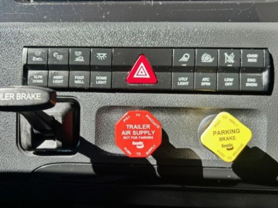 Dashboard controls of a Freightliner Cascadia cab showing hazard button and red/ yellow caps for trailer air supply and parking brake.